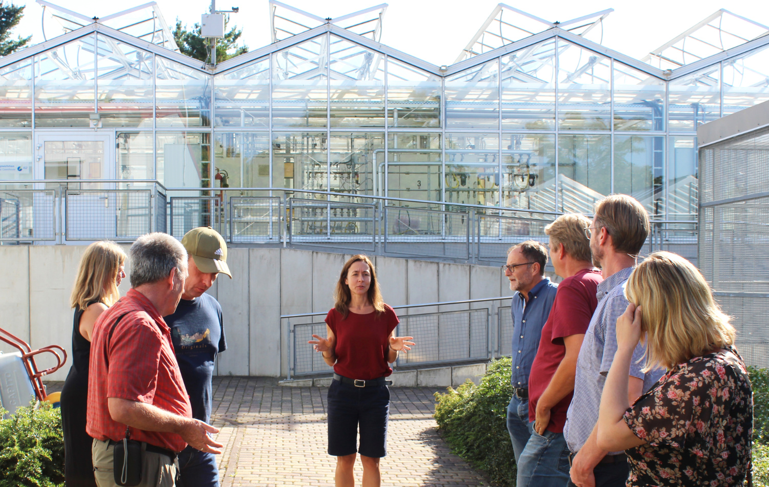 A group of people stands against the backdrop of the elevated gas exchange greenhouse.